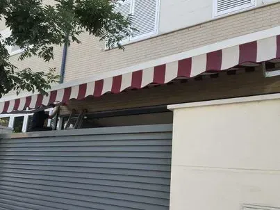 Una persona instalando un toldo a rayas rojas y blancas en un edificio.
