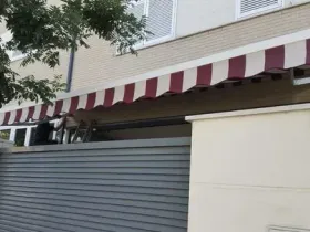 Una persona instalando un toldo a rayas rojas y blancas en un edificio.