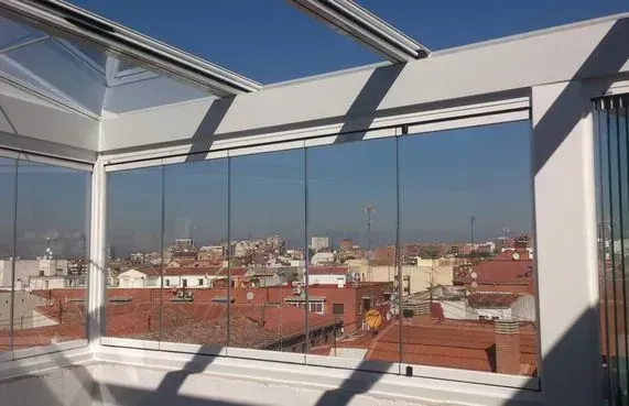 Balcón acristalado con vistas a un paisaje urbano con tejados rojos bajo un cielo brillante y soleado.