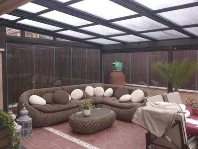 Zona de estar al aire libre con sofá seccional, bajo techo de cristal, paredes marrones.