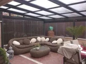 Zona de estar al aire libre con sofá seccional, bajo techo de cristal, paredes marrones.