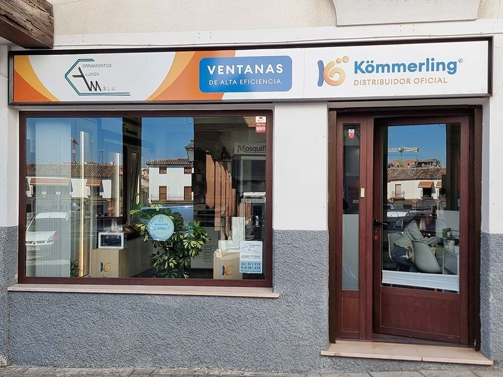 Local comercial con gran ventanal y puerta, venta de escaparates. Letrero naranja, azul y marrón sobre la puerta.