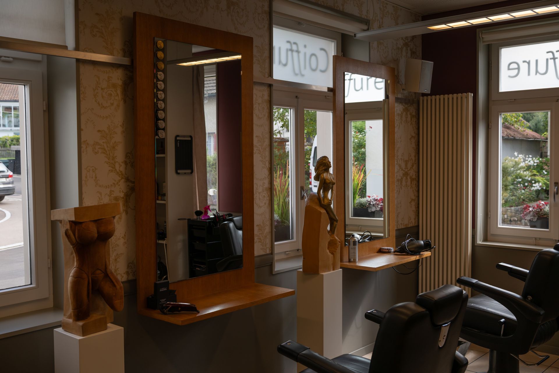 Innenraum eines Friseursalons mit drei Friseurstühlen, großen Spiegeln und Holzskulpturen.