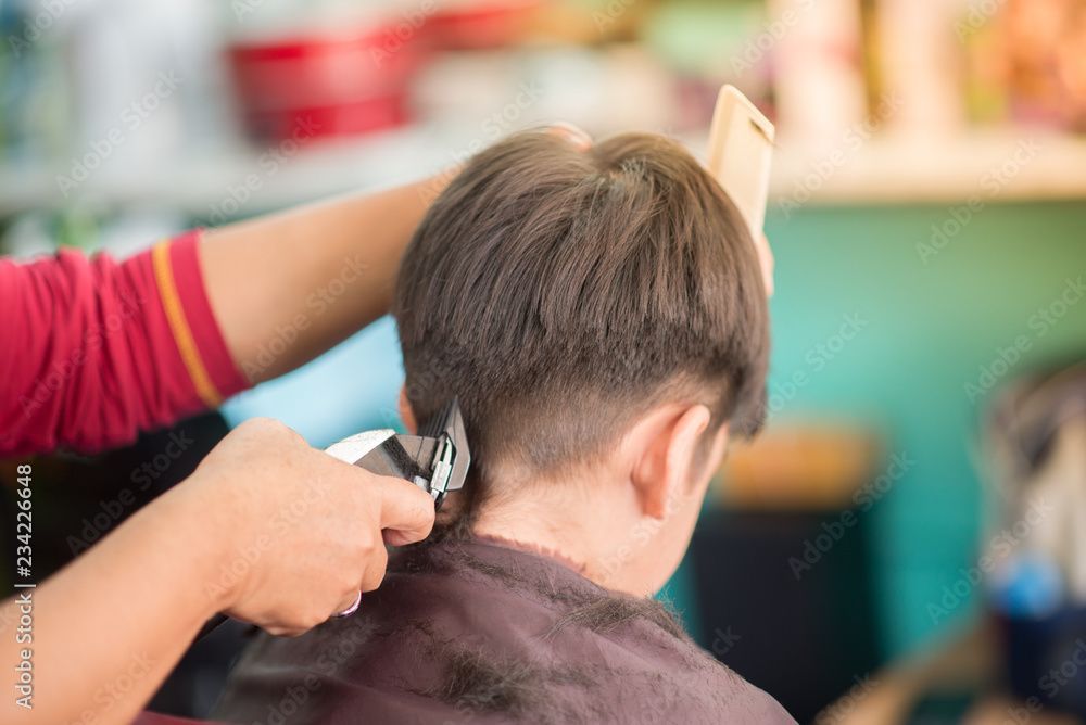 Friseur schneidet einem Kind mit einer Haarschneidemaschine die Haare. Hände halten Haarschneidemaschine und ein Telefon. Das Kind ist in einem Salon.