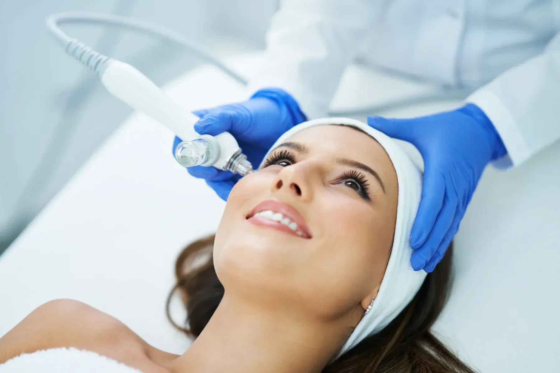 Mujer recibiendo tratamiento facial, sostenida por manos enguantadas.