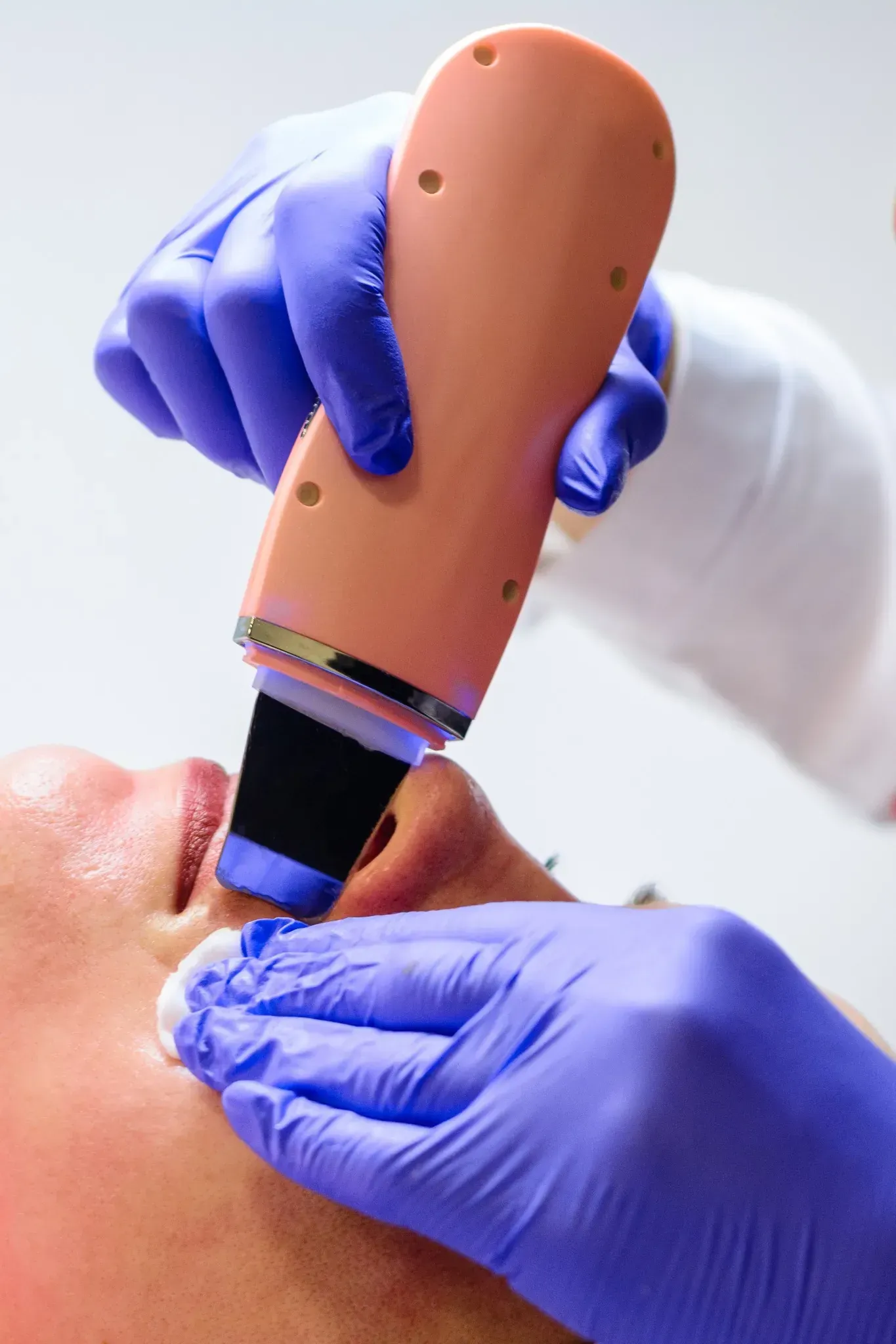 Persona que recibe un tratamiento facial con un depurador de piel sostenido por manos enguantadas.