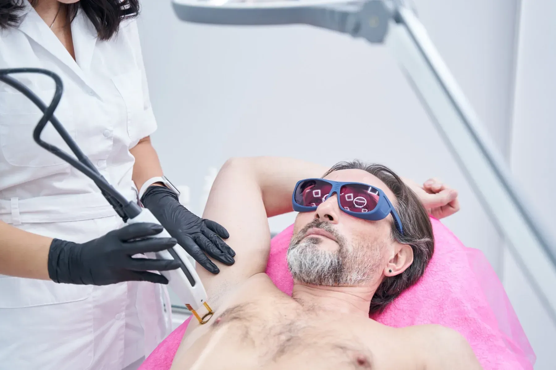 Hombre recibiendo depilación láser en las axilas. Técnico con guantes aplicando el láser al paciente.