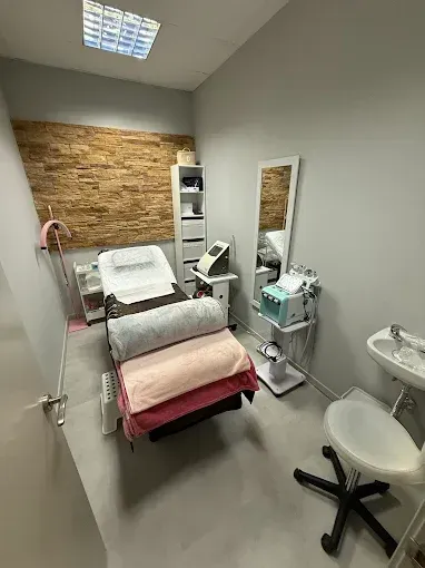 Sala de tratamiento con cama, equipo, espejo y pequeño lavabo.