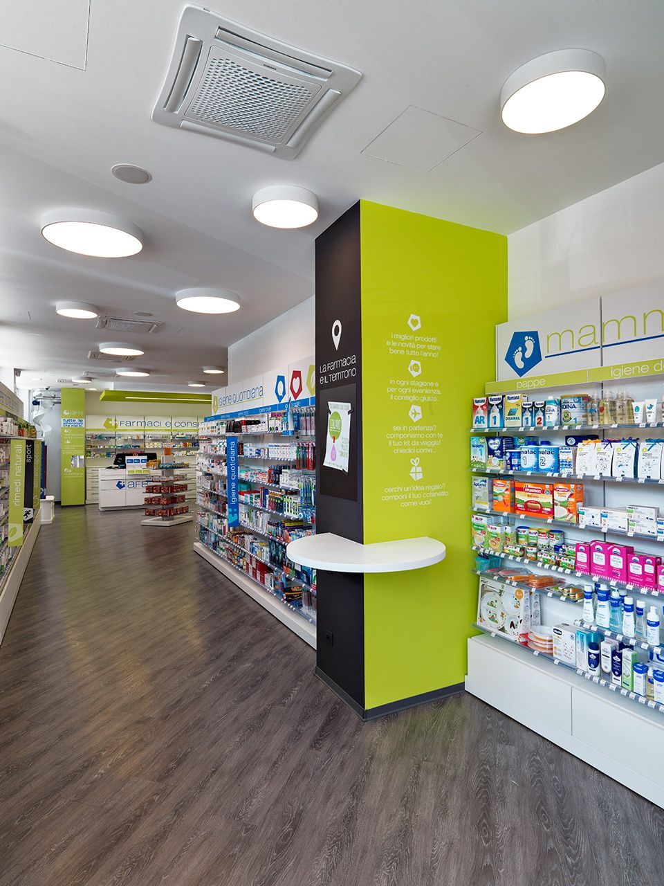 Vista interna di una farmacia con scaffali pieni di prodotti e una colonna verde e nera.