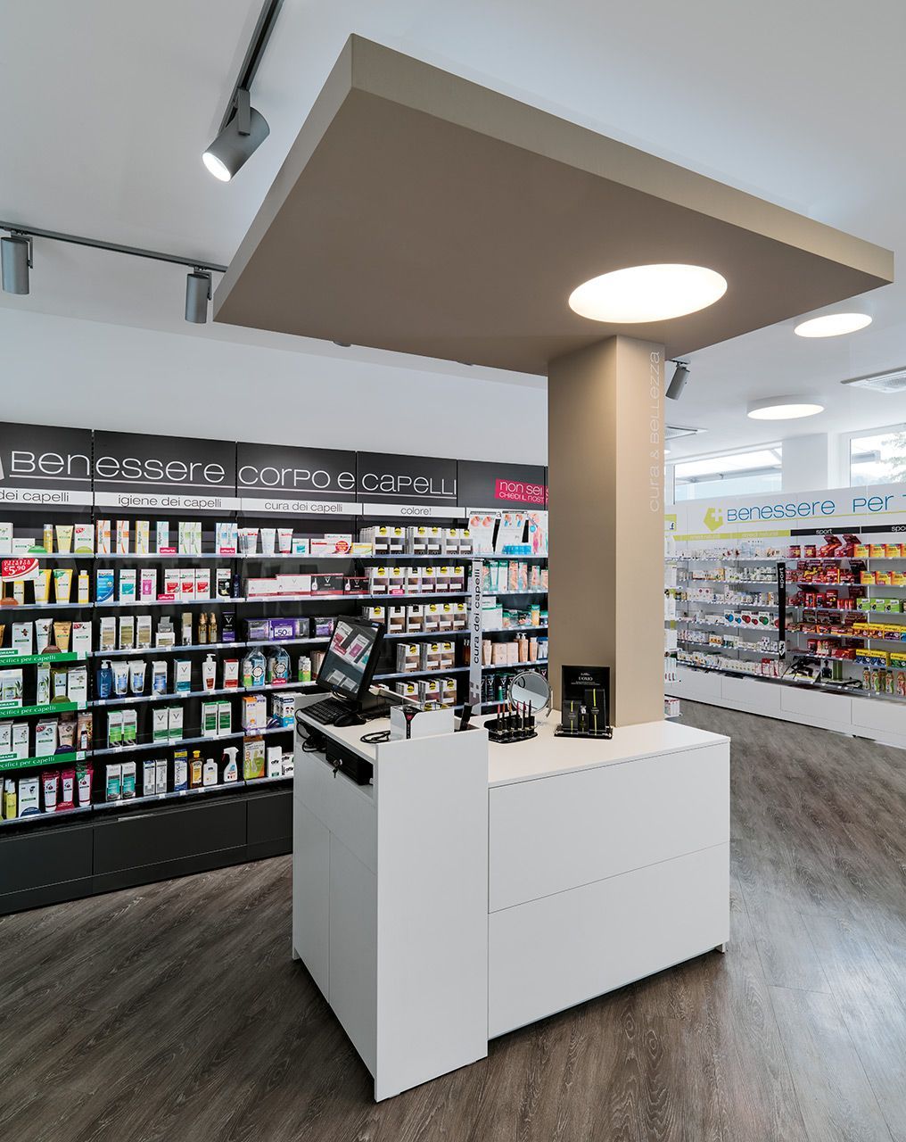 Interno di farmacia con bancone bianco, scaffali per i prodotti e illuminazione dall'alto.