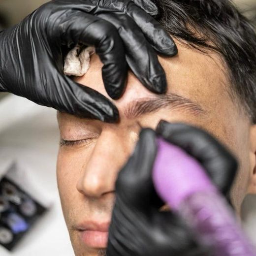 Un hombre se hace las cejas con una mujer que lleva guantes negros.