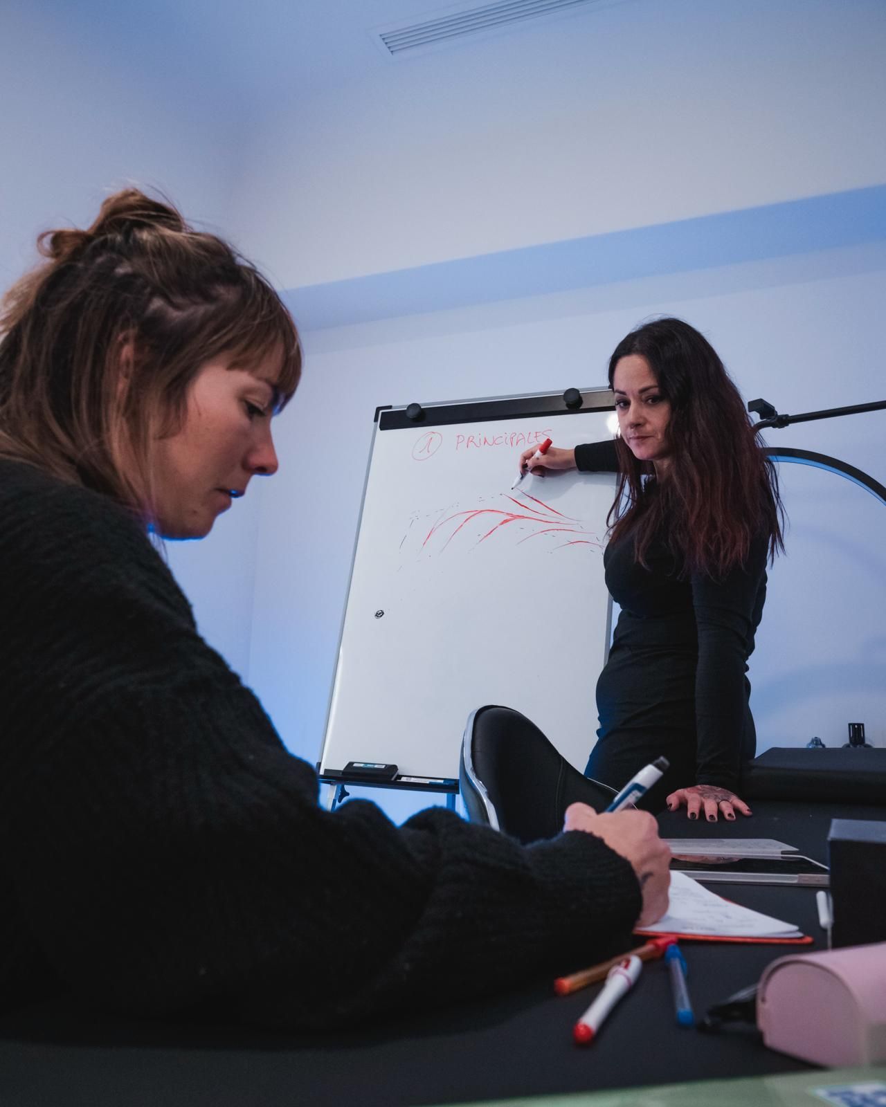 Dos mujeres están sentadas en una mesa escribiendo en una pizarra blanca.