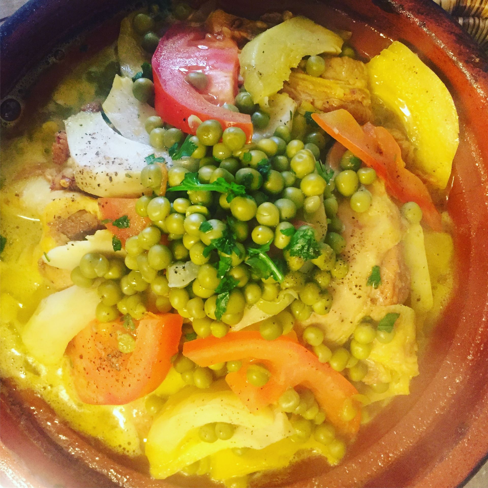 Tajine au poulet, petits pois, tomates, oignons, carottes et pommes de terre, cuit dans une cocotte en terre cuite.