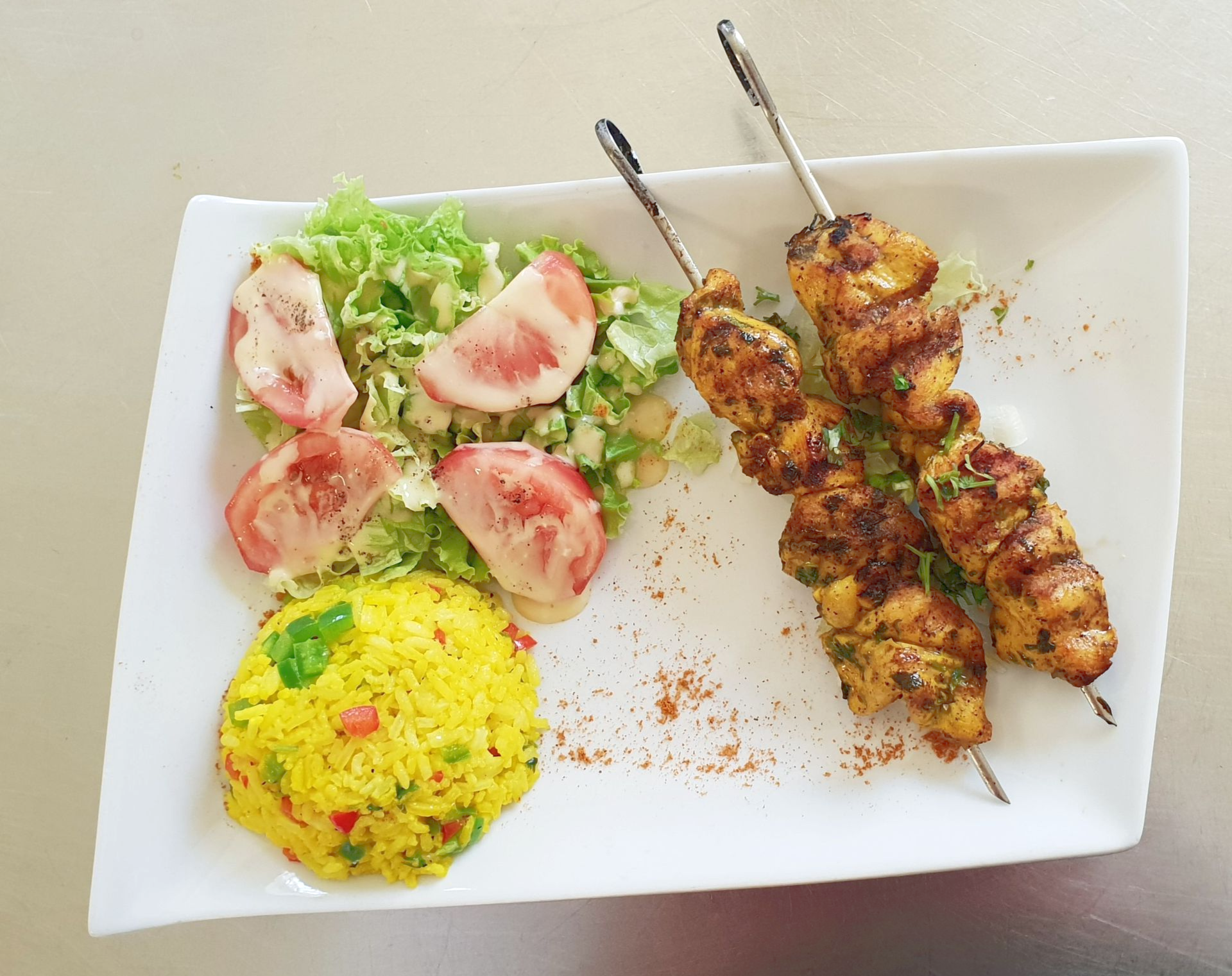 Brochettes de poulet grillé, riz jaune et salade sur une assiette blanche.
