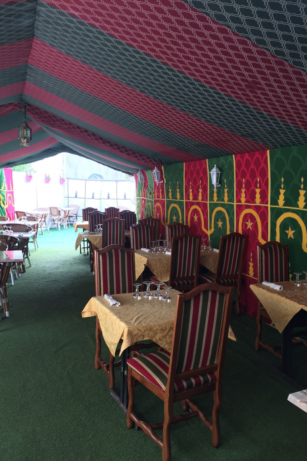 Intérieur du restaurant décoré de rouge, de vert et d'or, tables dressées et chaises disposées.