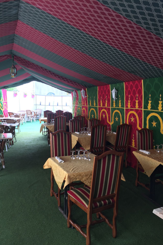 Intérieur du restaurant avec chaises rayées, nappes jaunes, panneaux de fenêtres en bois et plafond à motifs.
