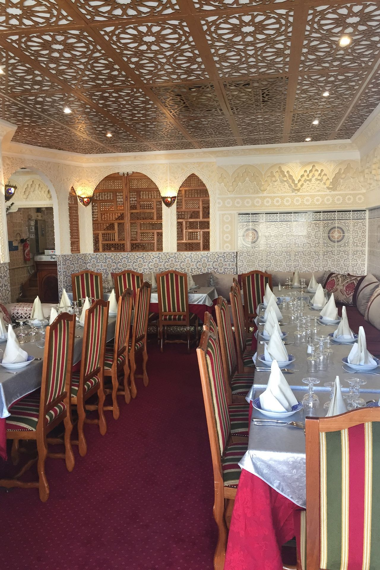 Intérieur de restaurant avec plafond orné, longues tables dressées pour les repas et détails décoratifs aux murs.