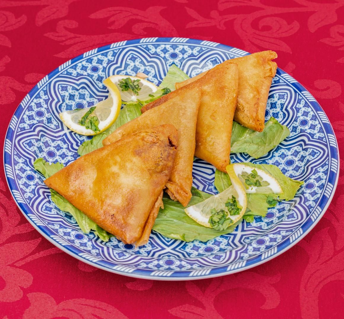 Petits gâteaux salés triangulaires, dorés et croustillants, présentés sur une assiette à motifs bleus, accompagnés de laitue et de tranches de citron.