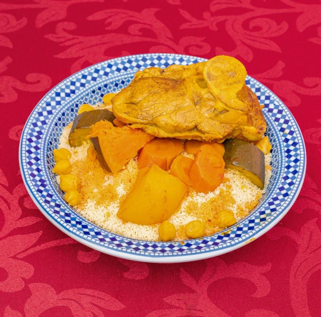 Plat de couscous au poulet, carottes, courge et pois chiches, servis dans un bol à bord bleu.
