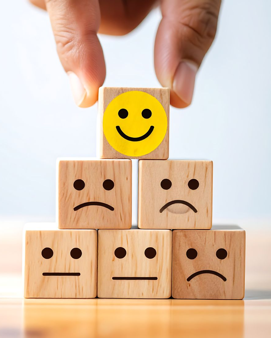 Une main dépose un bloc à visage souriant au sommet d'une pyramide de blocs à visage triste et neutre.