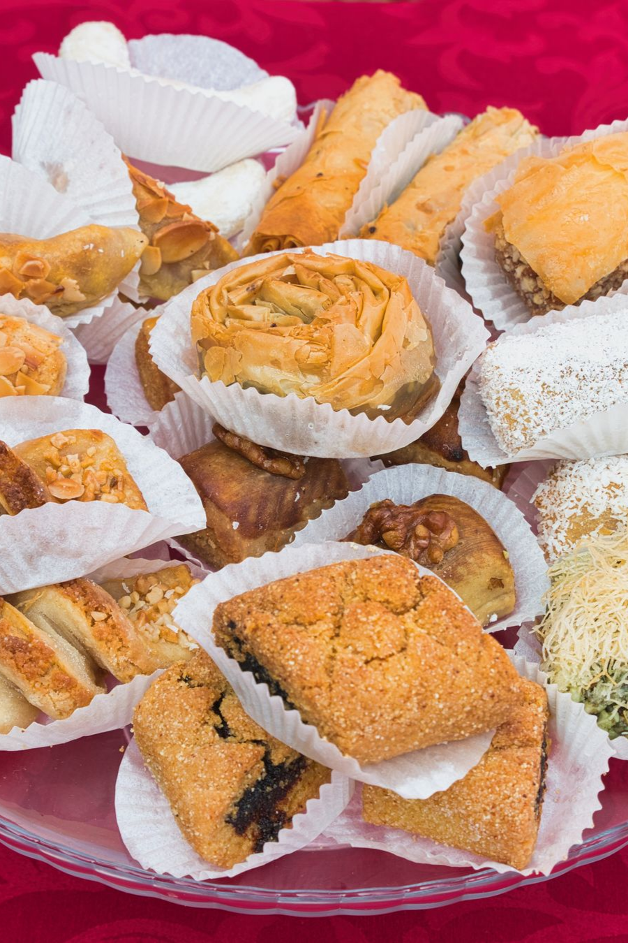 Une assiette de pâtisseries du Moyen-Orient variées, dont du baklava, sur une nappe rouge.