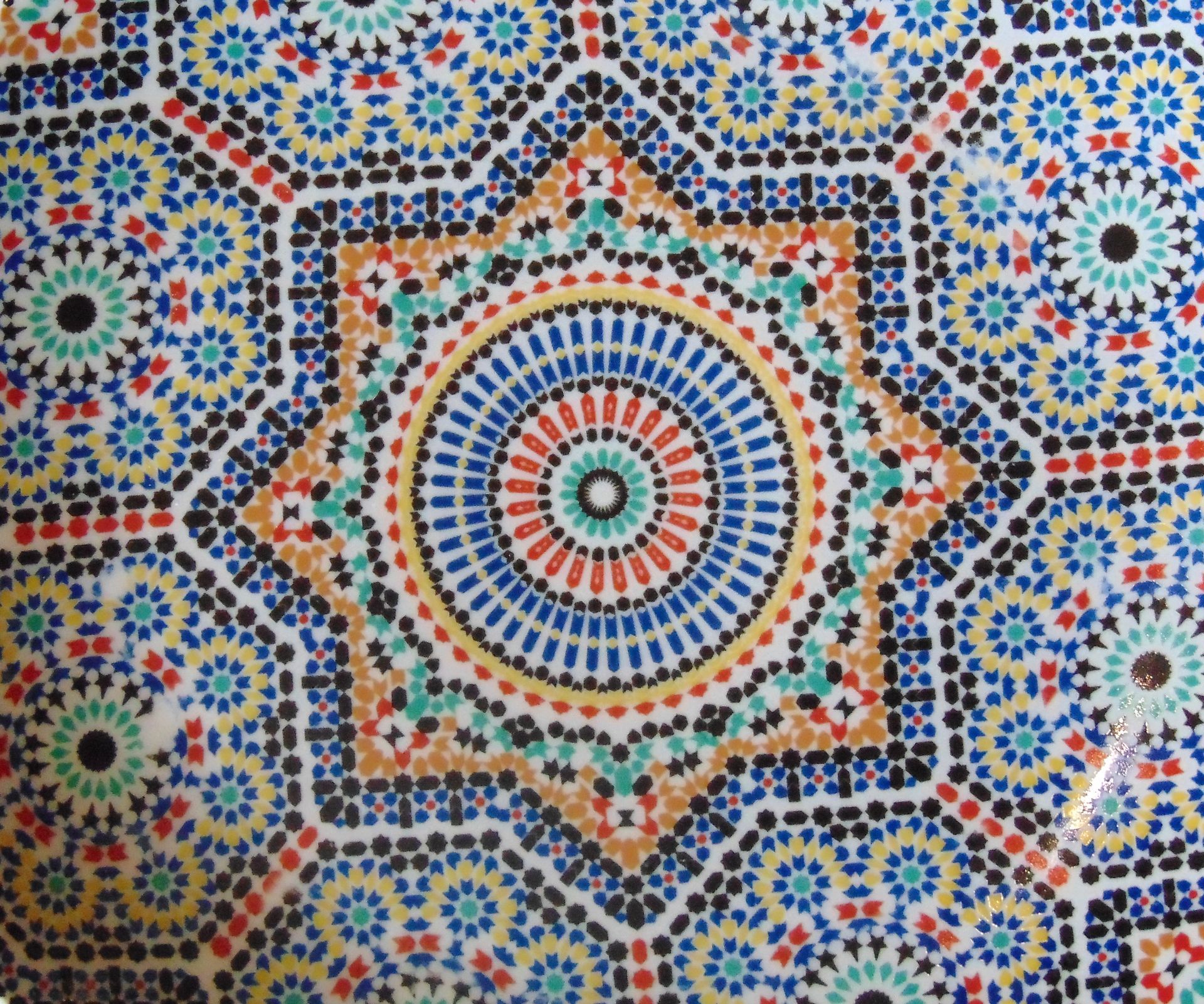 Motif de mosaïque en forme d'étoile à huit branches, composé de cercles concentriques et de formes géométriques bleues, rouges, vertes, noires et oranges.