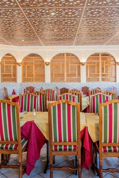 Intérieur du restaurant avec chaises rayées, nappes jaunes, panneaux de fenêtres en bois et plafond à motifs.