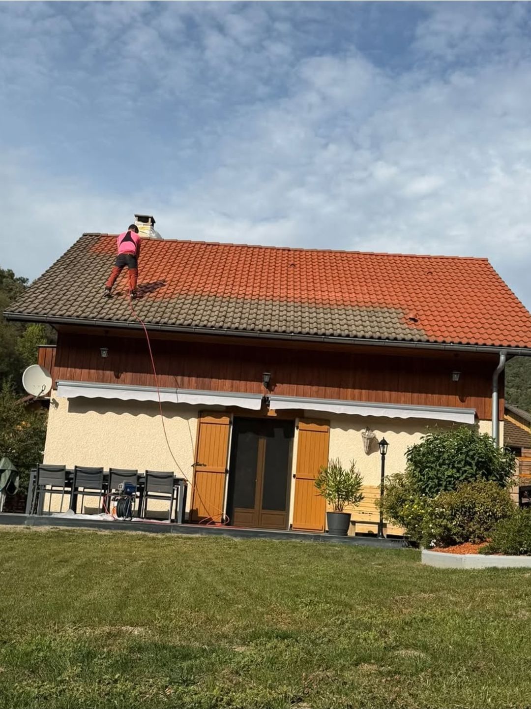 Une personne travaille sur le toit de tuiles rouges d’une maison, sous un ciel bleu.