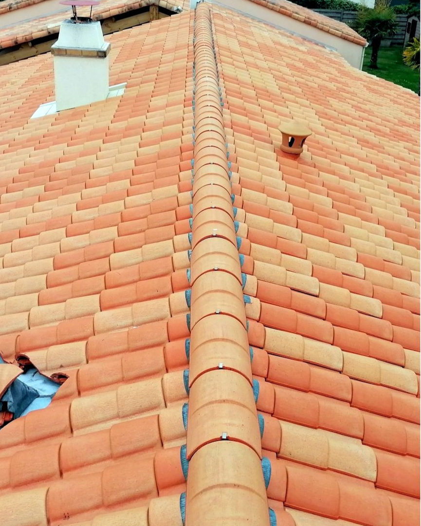 Toit d’une maison couvert de bardeaux bruns, avec des bordures vertes et une cheminée blanche, sous un ciel bleu dégagé