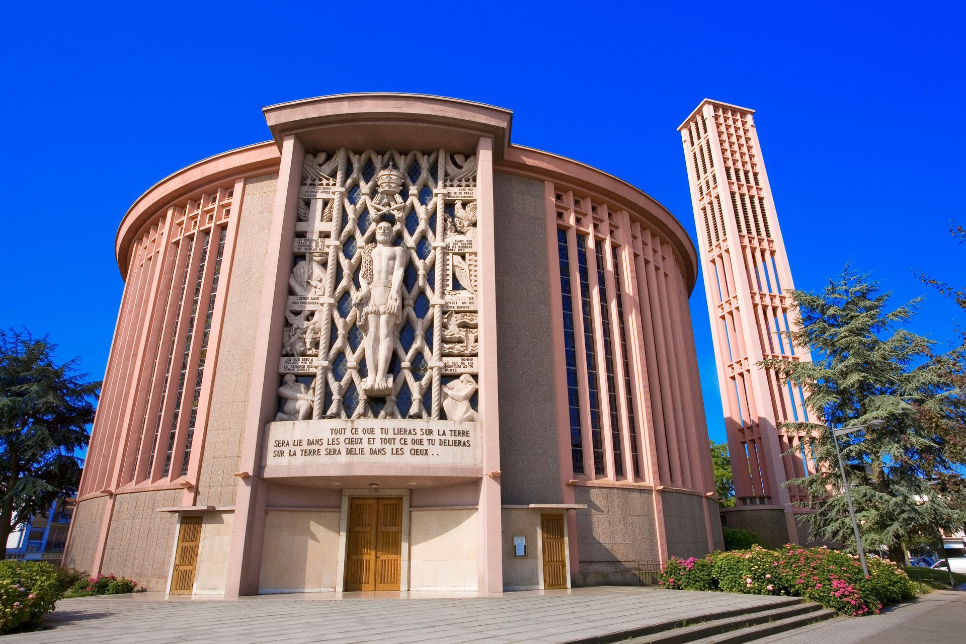 Église ronde et rose avec un haut clocher à treillis se détachant sur un ciel bleu.