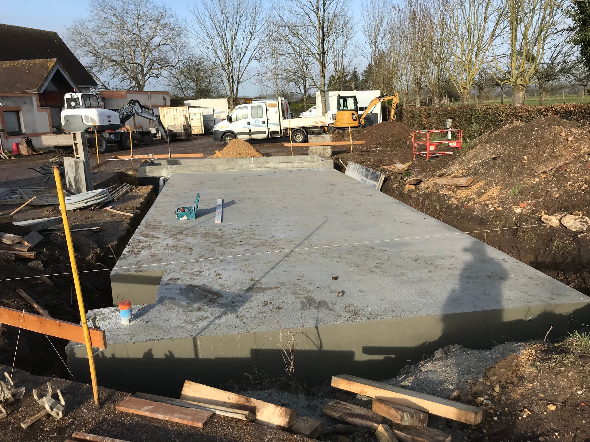 Fondation en béton coulée sur le chantier, avec des engins de chantier visibles en arrière-plan.