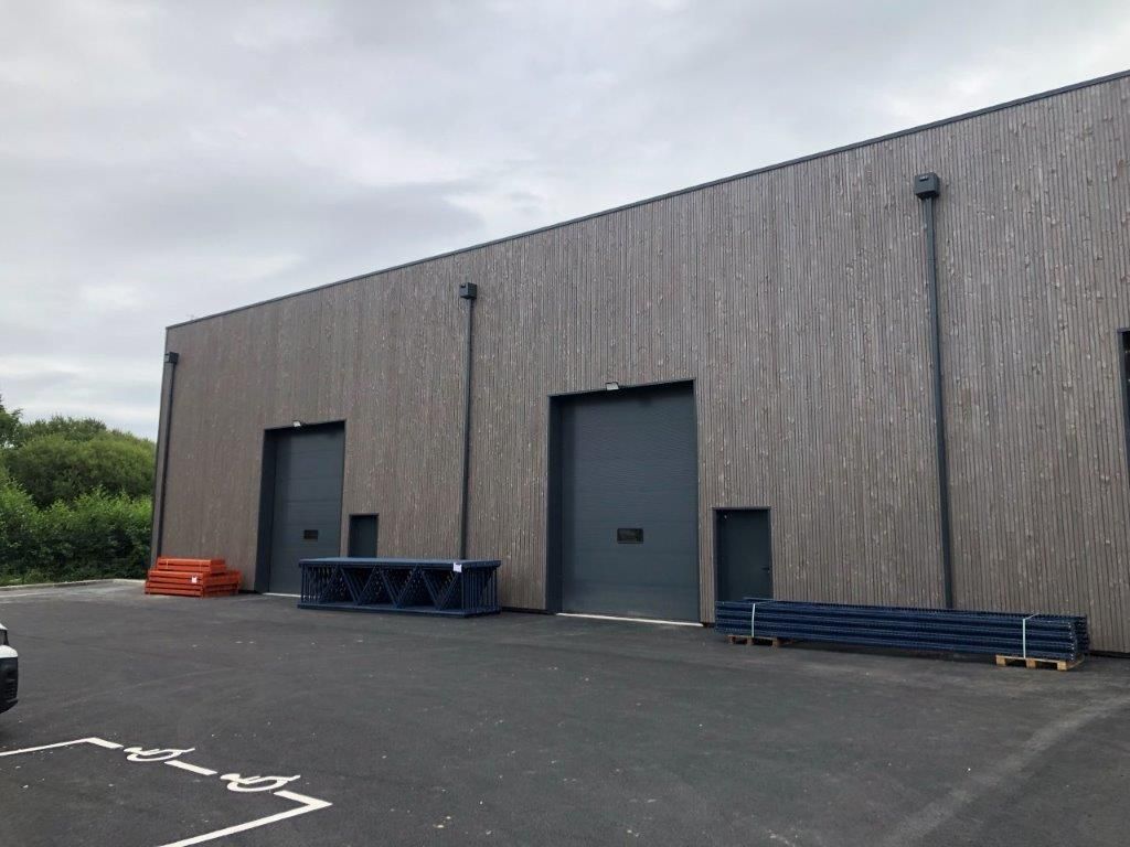 Bâtiment industriel moderne avec deux grandes portes de garage, un bardage en bois et un parking pavé.