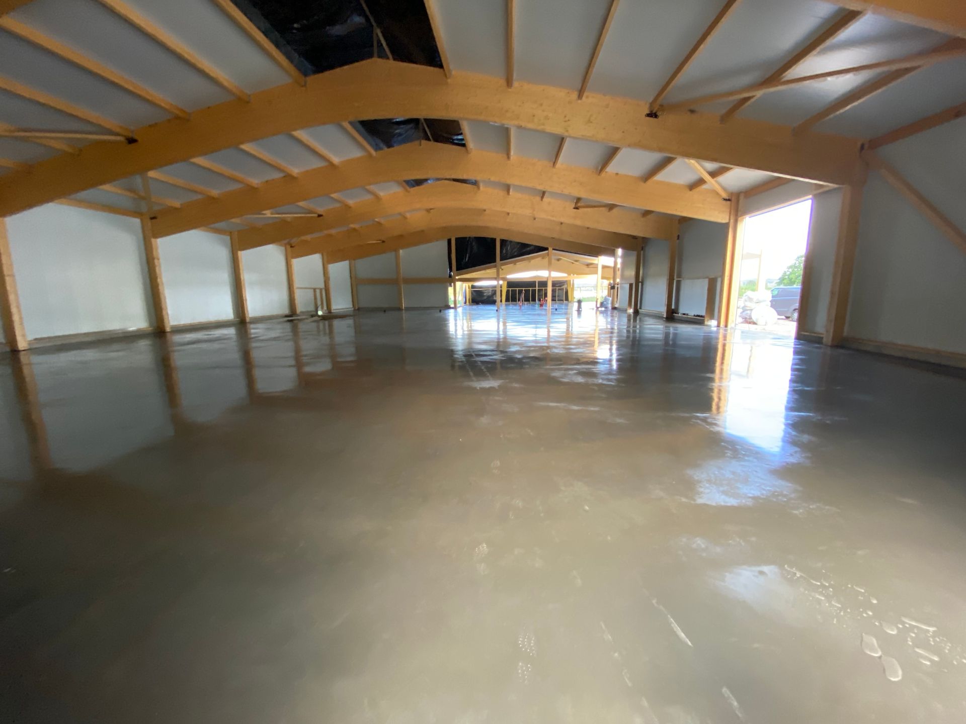 Intérieur d'un grand bâtiment avec un sol lisse et gris et des poutres en bois au plafond.