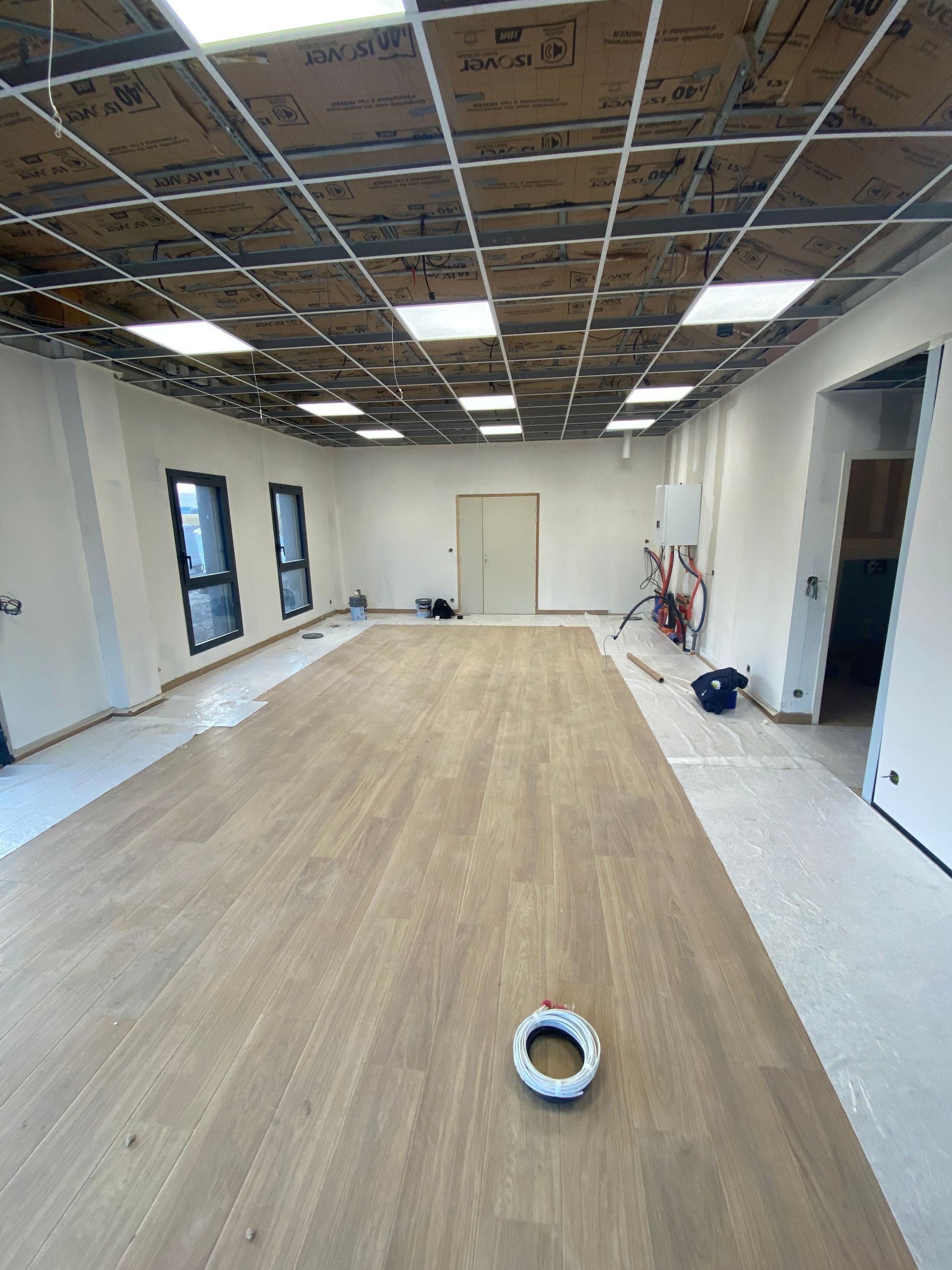 Pièce en construction avec parquet, murs blancs et plafond à ossature apparente avec éclairage.