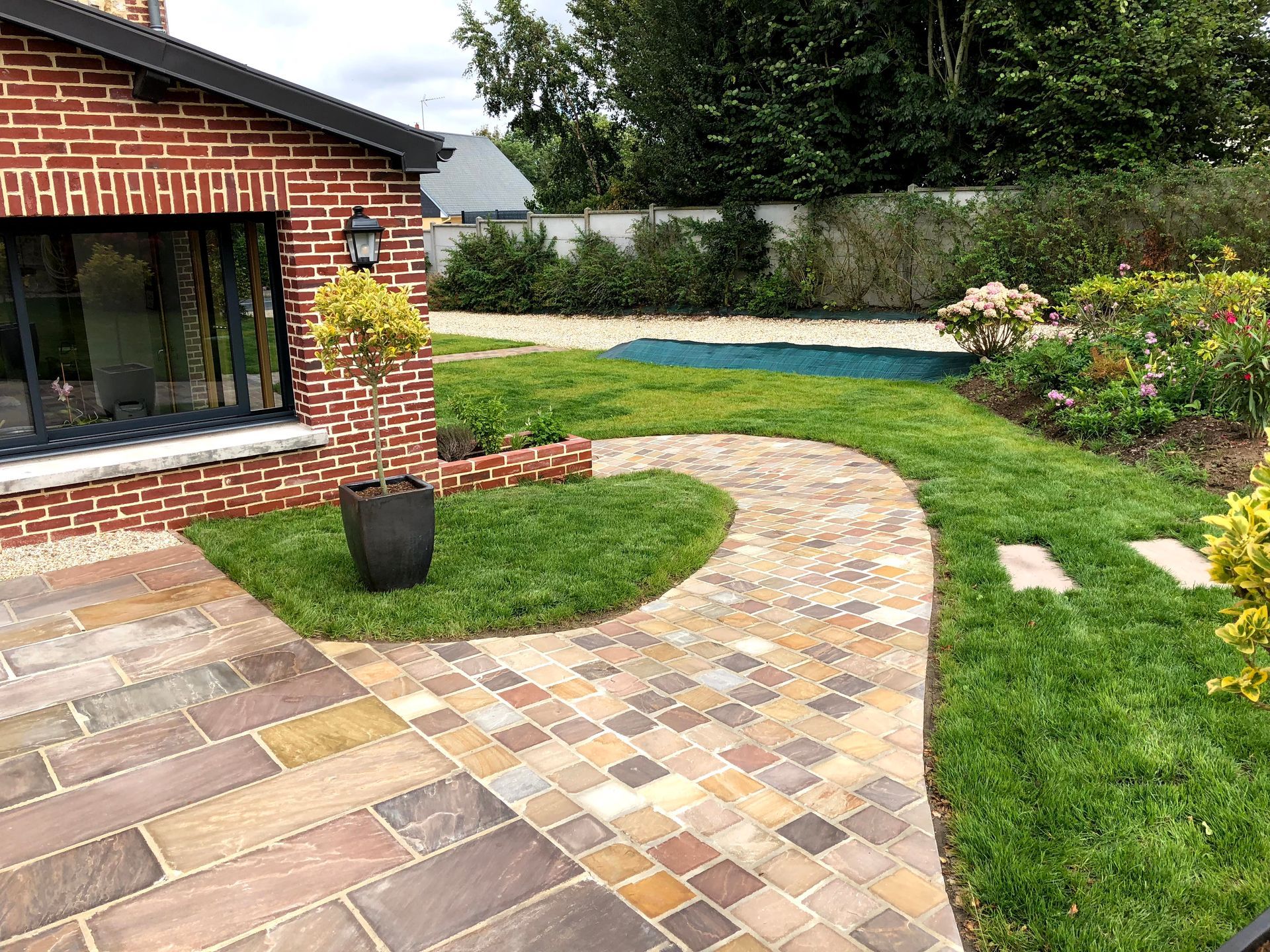 Extérieur d'une chaumière avec une terrasse grise en construction. Un râteau est posé sur la terrasse.