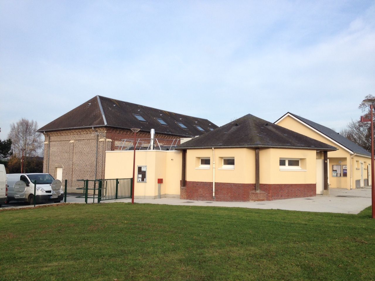 Bâtiments jaunes et en briques avec toit gris, camionnette garée et pelouse verte sous un ciel clair.