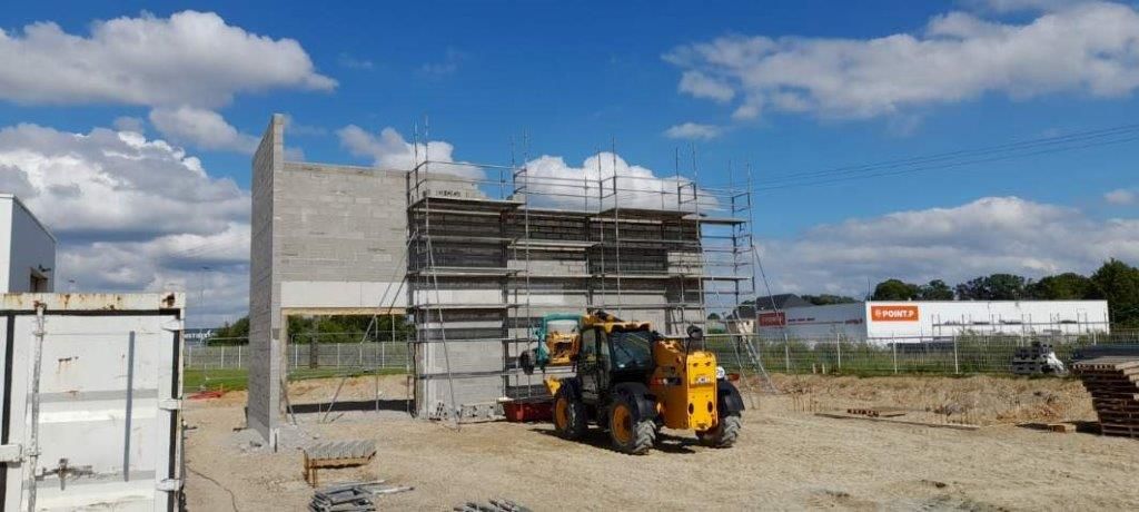 Chantier de construction avec structure partiellement édifiée, échafaudages et engins jaunes sous un ciel bleu.