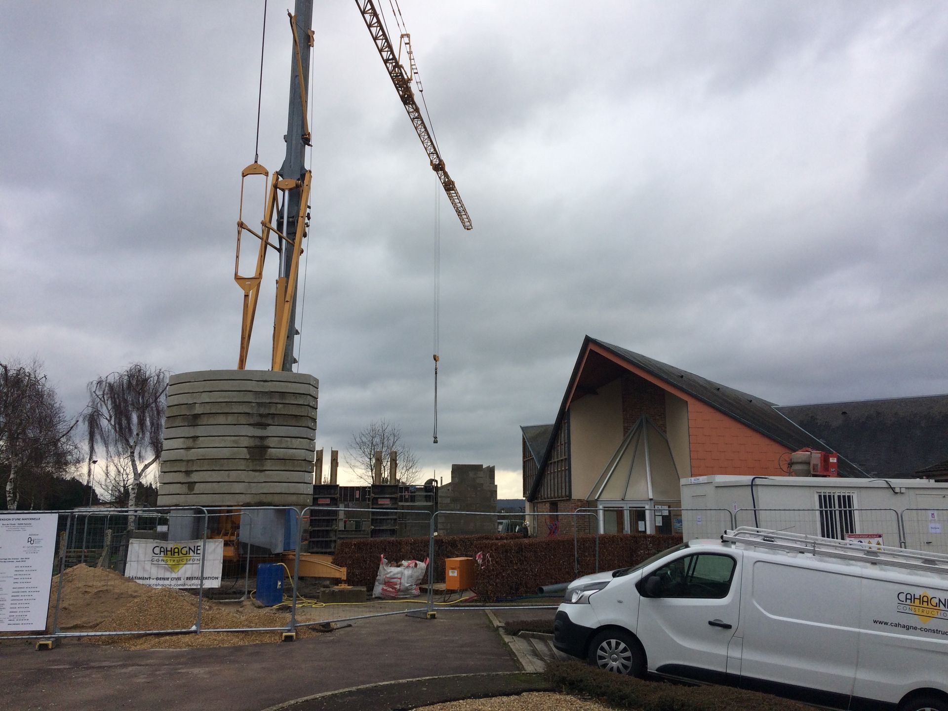 Chantier de construction avec grue soulevant des blocs de béton ; bâtiment en cours de construction, ciel nuageux.