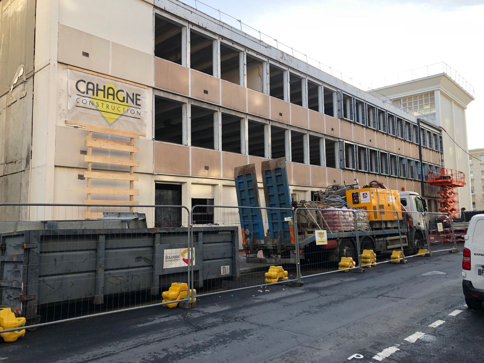 Bâtiment en construction, avec engins de chantier et bennes à gravats dans la rue. Le panneau Cahagne est visible.