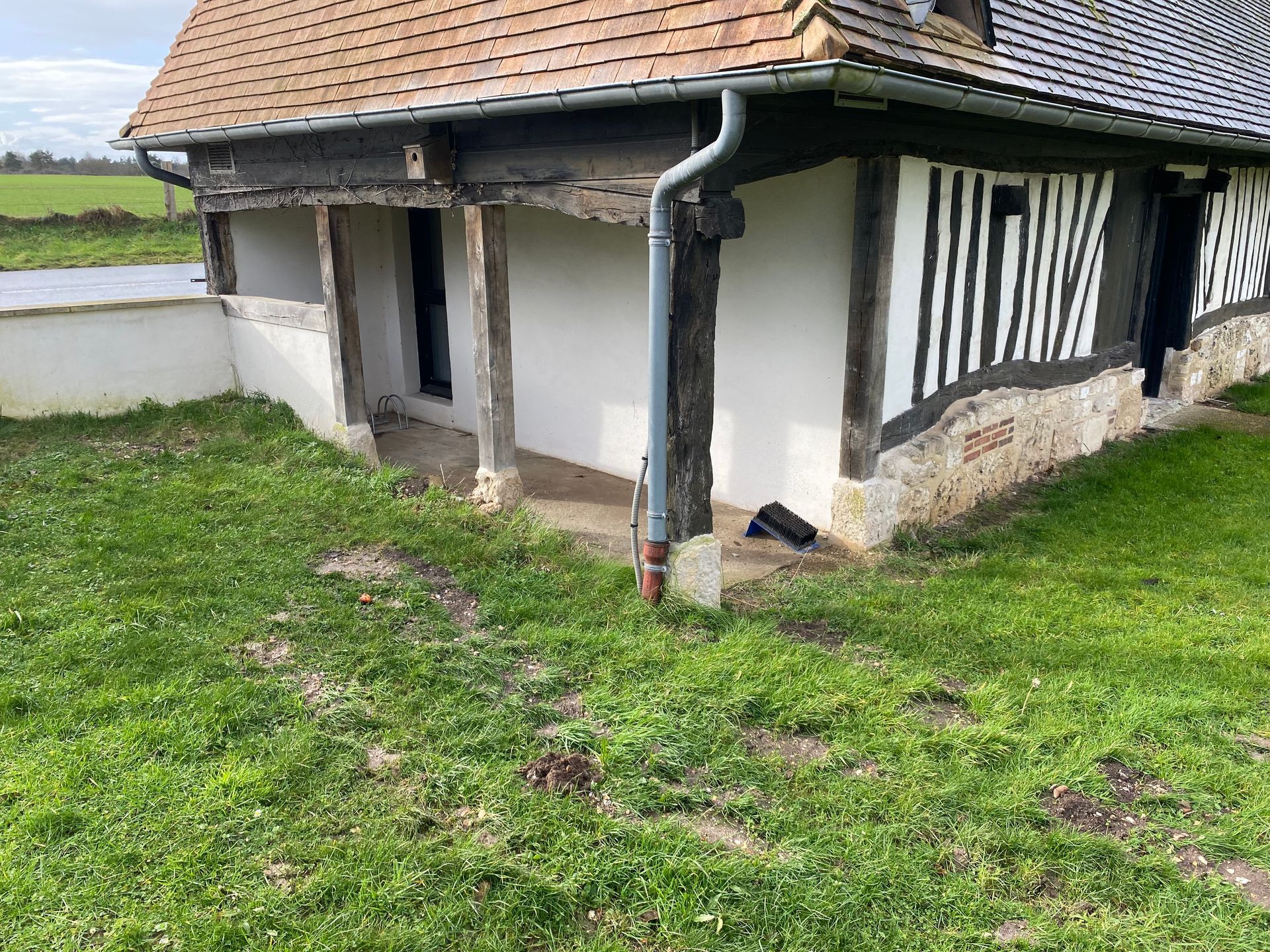 Bâtiment à colombages avec toit brun et murs en plâtre blanc, premier plan herbeux.
