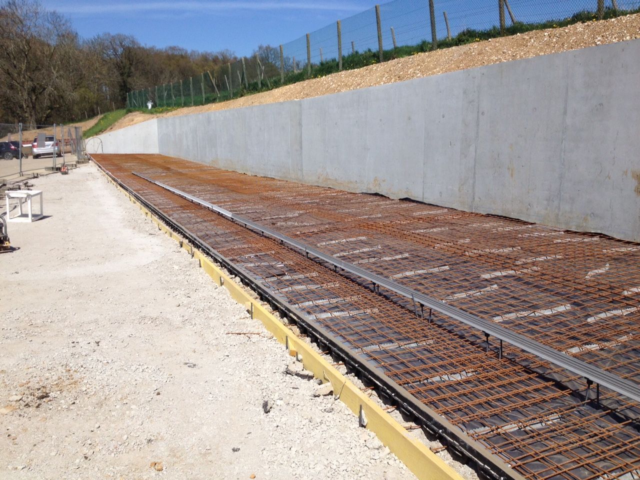 Chantier de construction avec treillis d'armature préparé pour le béton, à côté d'un mur de soutènement.