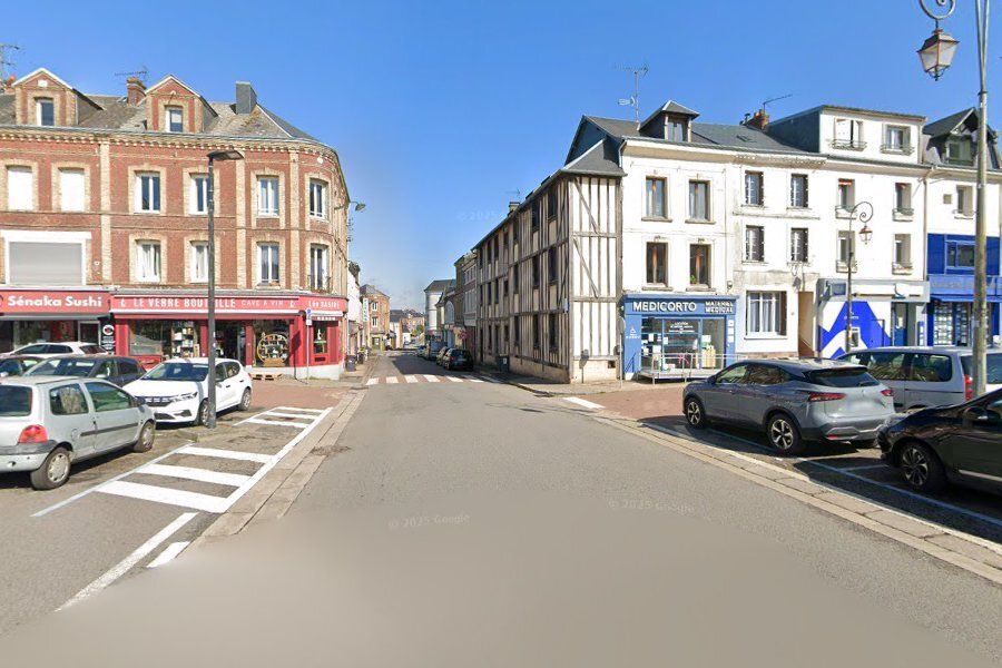 Scène de rue dans une ville européenne avec des magasins et des voitures garées.