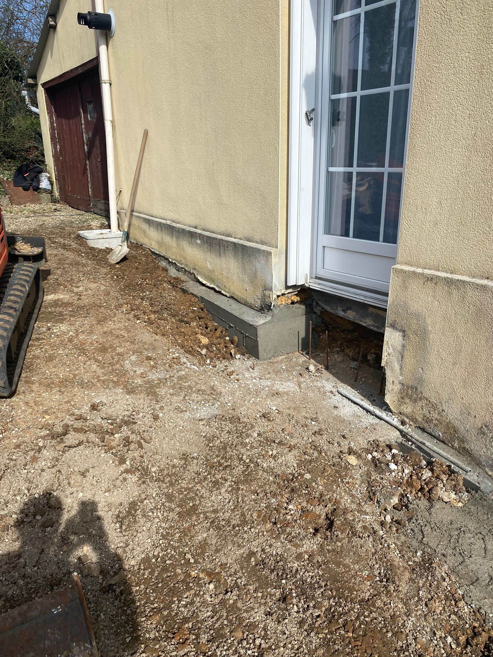 Extérieur d'un bâtiment avec allée de gravier. Nouvelle dalle de béton devant une porte. Travaux de construction en cours.