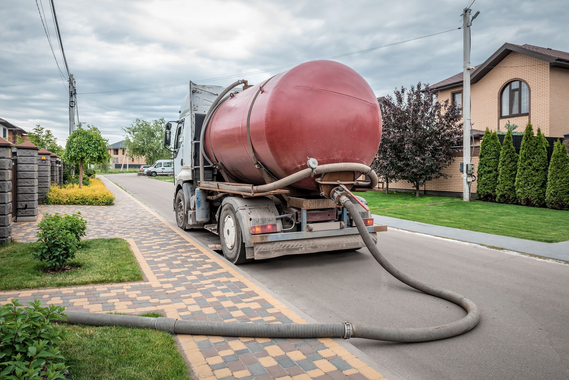 Un camion-citerne vide une grande cuve rouge à travers un tuyau dans une rue de banlieue