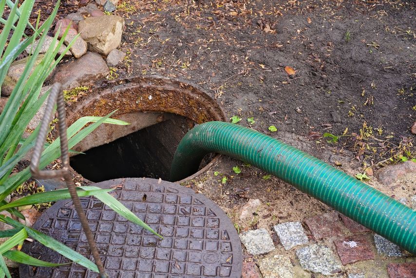 Bouche d'égout ouverte dans la terre par laquelle un tuyau vert passe.