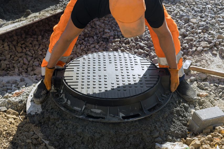 Ouvrier en tenue de sécurité orange installant une plaque d'égout sur un chantier de gravier