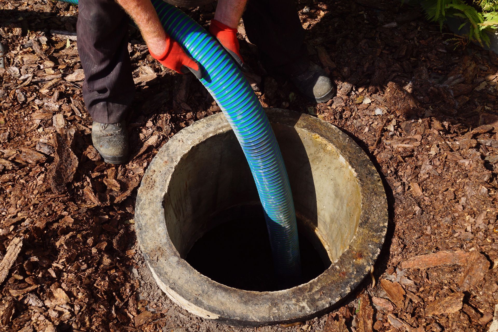 Personne descendant un tuyau bleu dans un puits en béton à l'extérieur