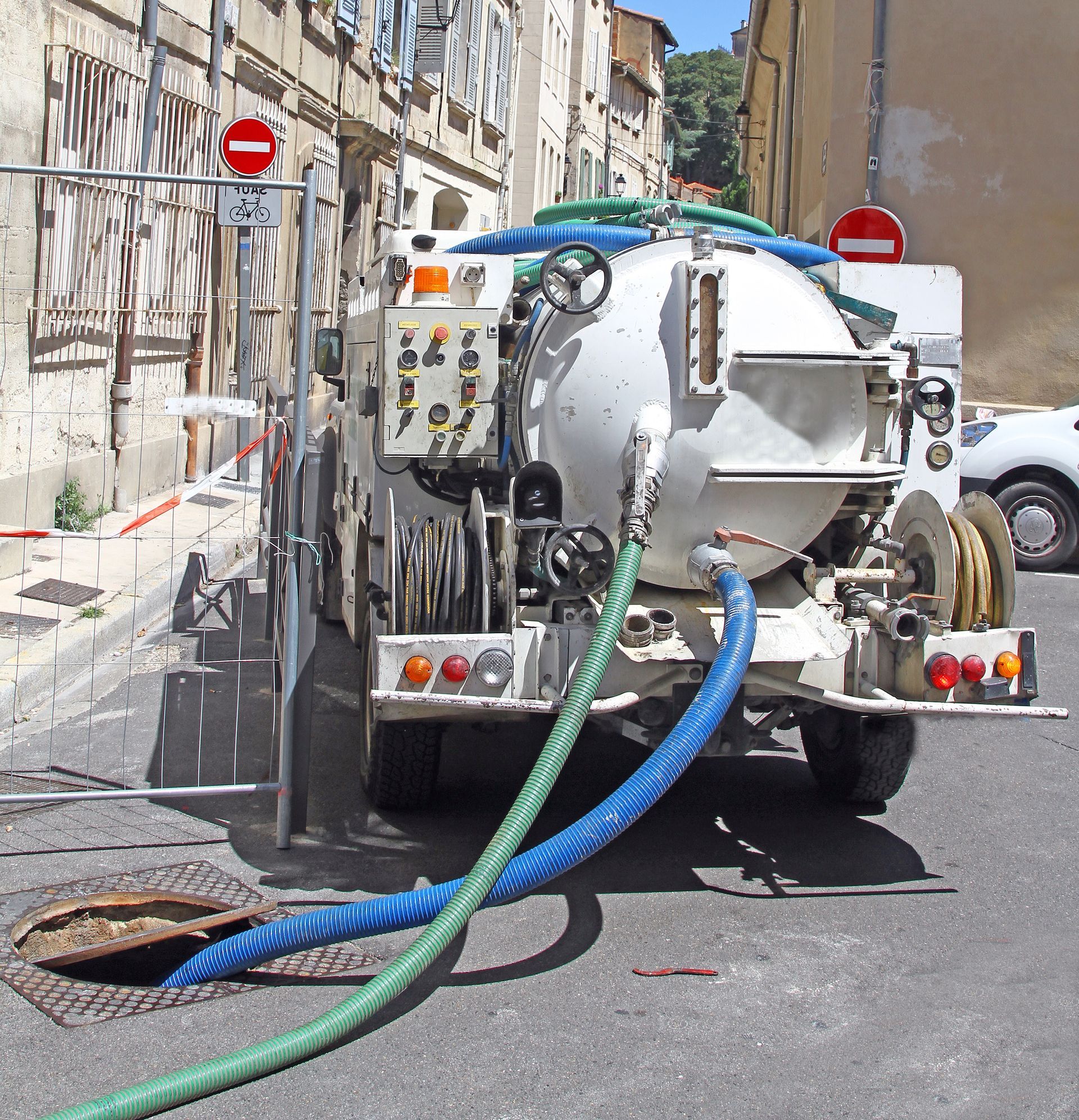 Camion aspirateur blanc avec tuyaux nettoyant une rue étroite entre de vieux bâtiments.