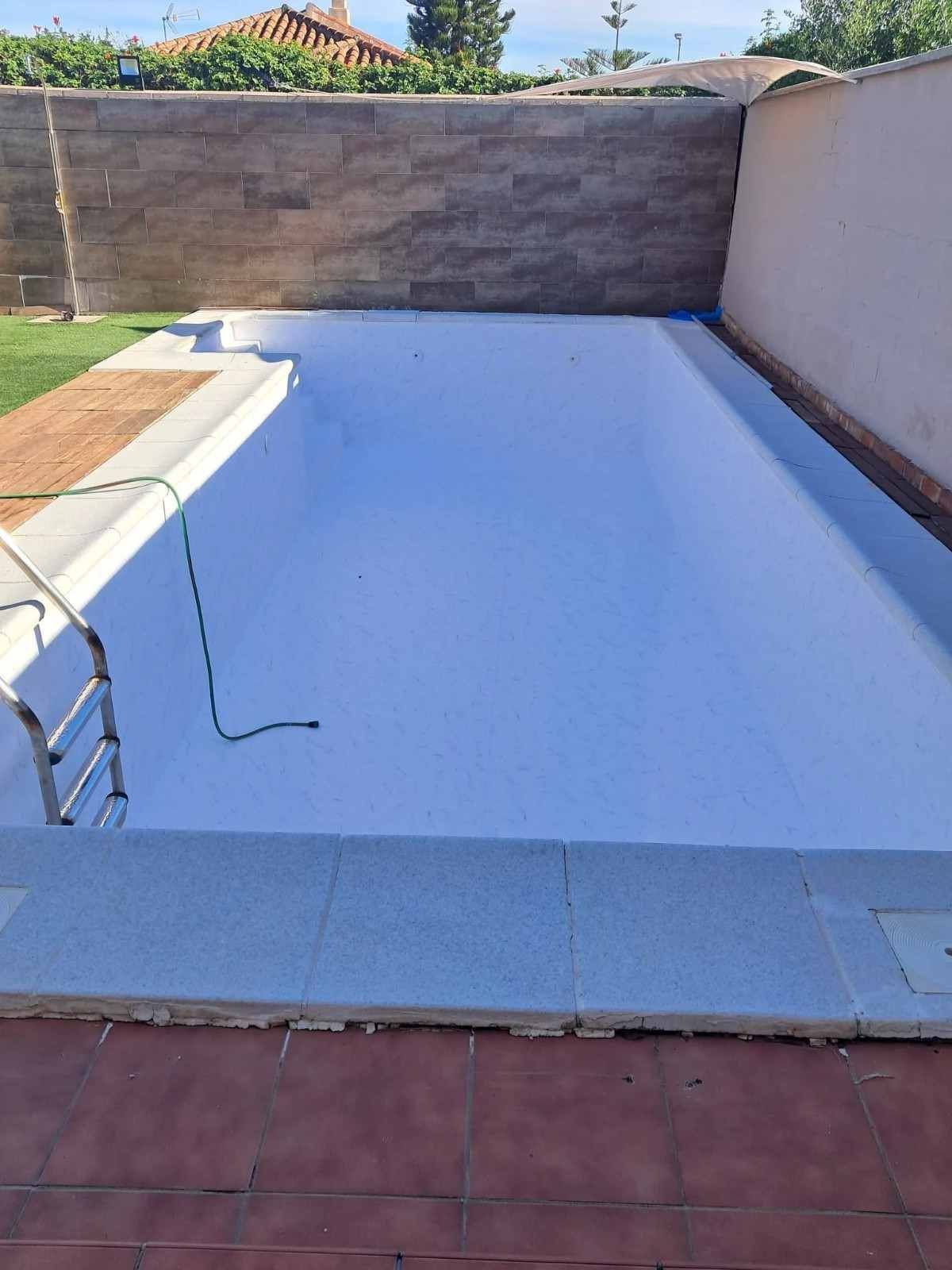 Piscina rectangular vacía con revestimiento blanco y muros de piedra y patio alrededor.