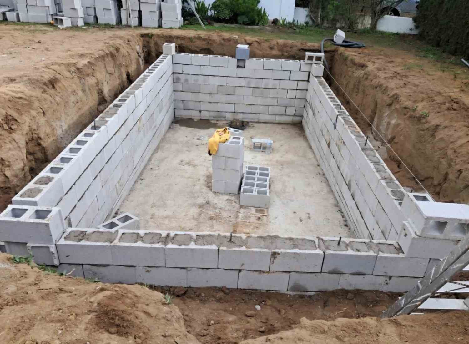 Cimentación parcialmente construida con bloques de hormigón en una obra, con un terreno de tierra y un suelo de hormigón.